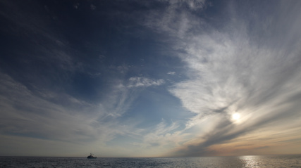 A fishing boat on the water in the distance with the setting sun in the background.
