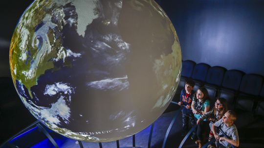 Four students looking a Earth projected on a large sphere.